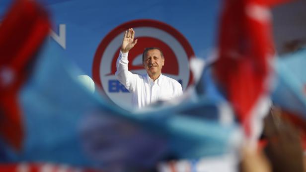 Recep Tayyip Erdoğan winkt vor einem Wahlkampflogo.