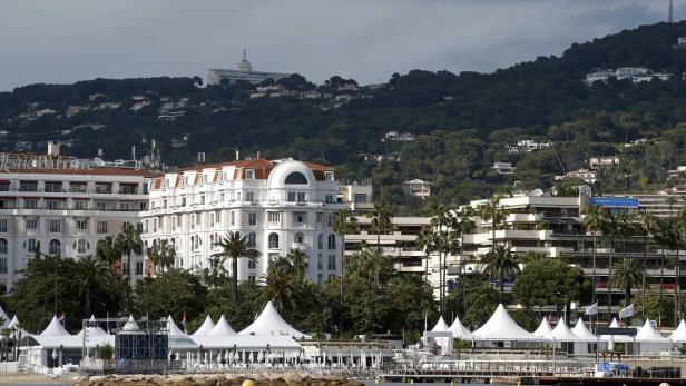 Blick auf Cannes mit weißen Zelten am Strand und einem bewaldeten Hügel im Hintergrund.