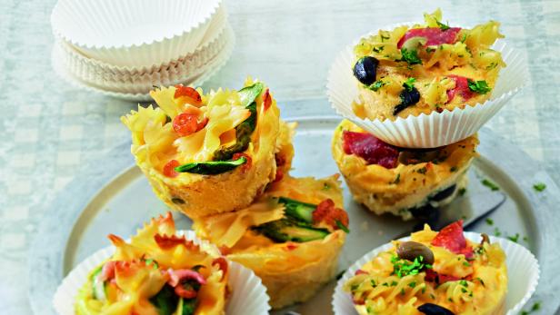 Mehrere herzhafte Pasta-Muffins mit Gemüse und Oliven auf einem Teller.