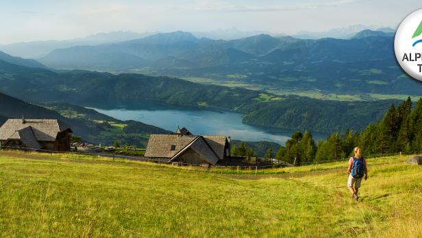 Eine Wanderin auf dem Alpe Adria Trail mit Blick auf einen See und die Berge.