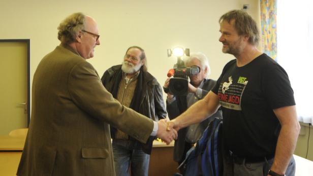 Zwei Männer geben sich die Hand, während ein Kameramann die Szene filmt.