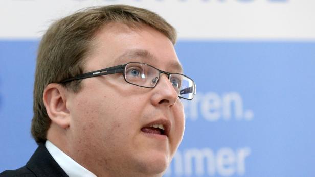 Ein Mann mit Brille spricht vor einem hellblauen Hintergrund.
