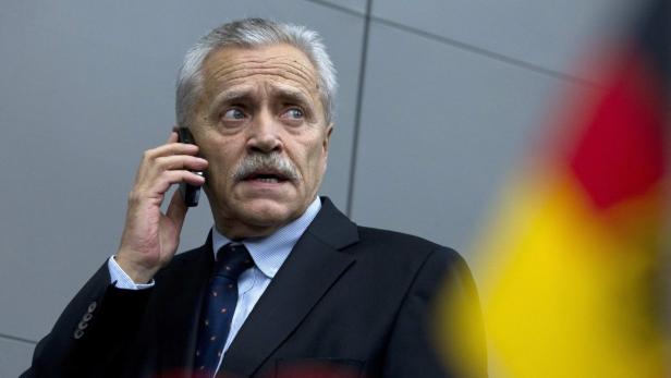 Ein Mann im Anzug telefoniert mit einem Mobiltelefon vor einer Deutschlandflagge.
