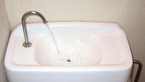 Wasser läuft aus einem silbernen Wasserhahn in ein weißes Waschbecken.