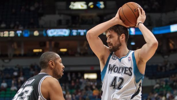 Ein Basketballspieler der Timberwolves hält den Ball über dem Kopf, während ein Gegenspieler ihn beobachtet.