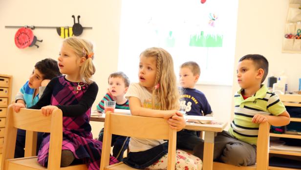 Eine Gruppe von Kindern sitzt an einem Tisch und schaut aufmerksam in eine Richtung.