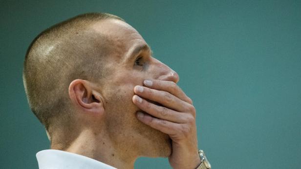 Ein Mann mit kurzem Haar hält seine Hand vor den Mund.