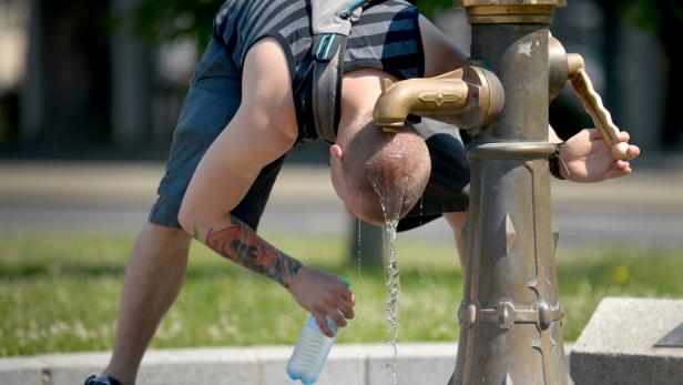 Ein Mann beugt sich über einen Brunnen, um Wasser zu trinken und eine Flasche zu füllen.