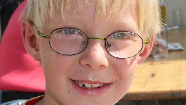 Ein lächelnder Junge mit blonden Haaren und Brille.