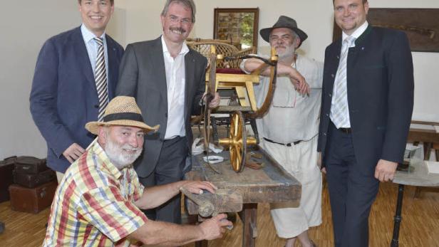 Eine Gruppe von Männern steht um eine Werkbank mit einem hölzernen Spielzeugwagen.