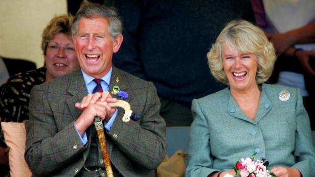 König Charles und Königin Camilla lachen herzlich, während sie nebeneinander sitzen.