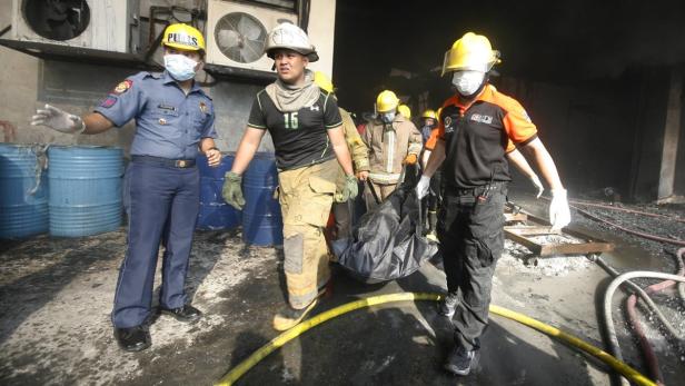 Feuerwehrleute und ein Polizist tragen eine Leiche aus einem ausgebrannten Gebäude.