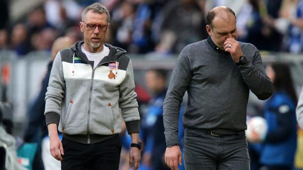 Zwei Männer, vermutlich Trainer, stehen während eines Spiels am Spielfeldrand.