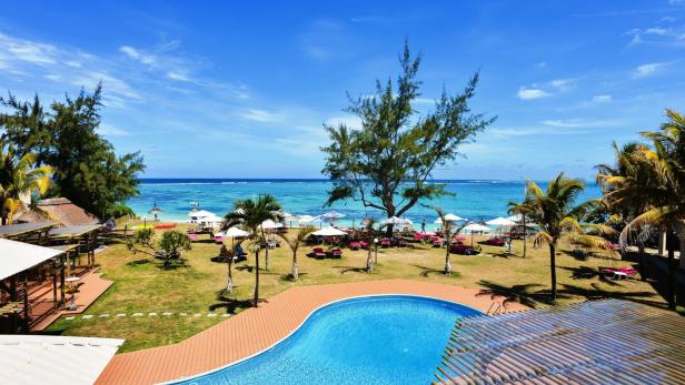Ein Resort mit Pool, Rasenfläche, Palmen und Blick auf den Strand.