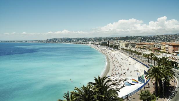 Ein Panoramablick auf den Strand von Nizza mit vielen Menschen und türkisfarbenem Wasser.