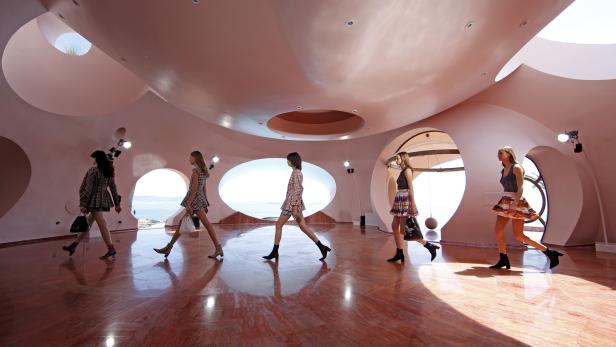 Mehrere Models laufen in einem rosafarbenen Gebäude mit Meerblick über den glänzenden Boden.