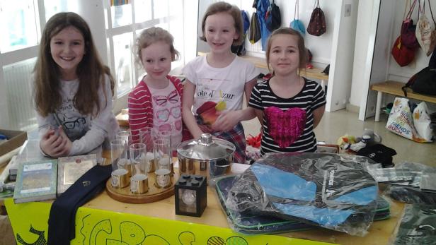 Vier Mädchen stehen an einem Tisch mit verschiedenen Gegenständen zum Verkauf.