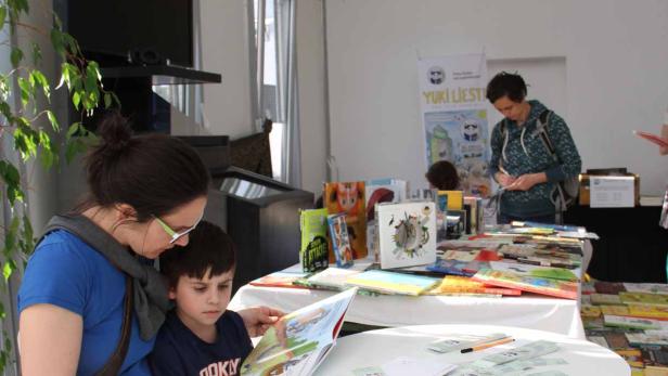 Eine Frau liest mit einem Kind ein Bilderbuch an einem Stand mit Büchern.