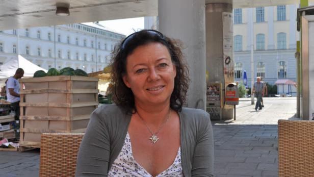 Eine Frau sitzt im Freien vor einem Gebäude und lächelt.