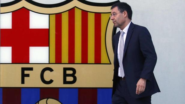 Ein Mann im Anzug geht vor dem Wappen des FC Barcelona entlang.