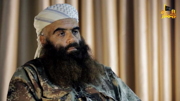 Ein Mann mit Bart und Tarnkleidung trägt eine Kopfbedeckung.