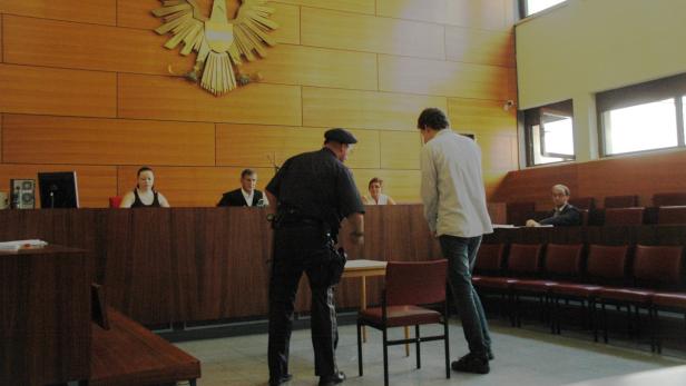 Ein Gerichtssaal mit Richtern, einem Angeklagten und einem Justizbeamten.