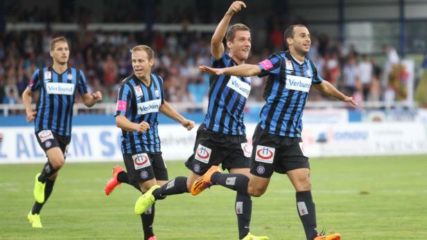 Mehrere Fußballspieler in blau-schwarz gestreiften Trikots jubeln auf dem Rasen.
