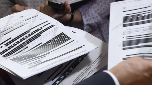 Personen betrachten Dokumente mit geschwärzten Passagen.