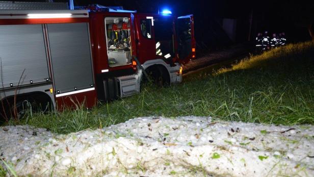 Ein Feuerwehrwagen steht nachts auf einer Wiese mit Hagel bedeckt.