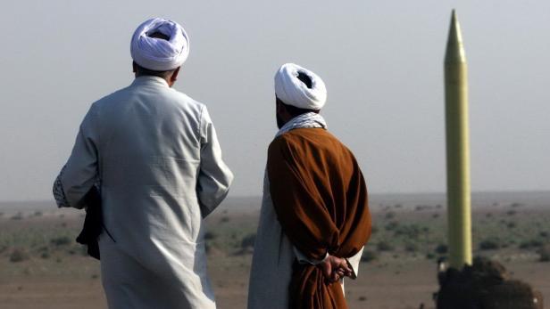 Zwei Männer mit Turbanen betrachten eine Rakete in einer Wüstenlandschaft.