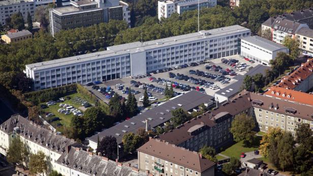 Luftaufnahme eines großen Bürogebäudes mit Parkplatz in einer städtischen Umgebung.
