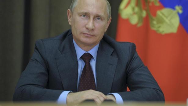 Wladimir Putin sitzt an einem Tisch vor einer russischen Flagge.