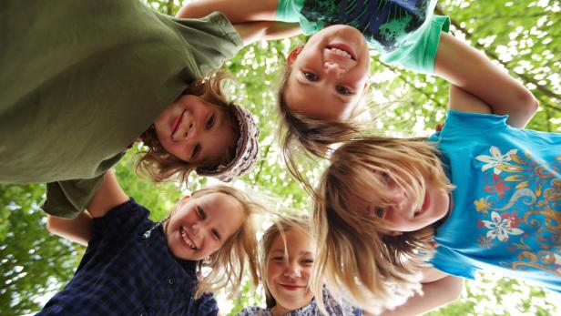 Fünf lachende Mädchen stehen im Kreis und schauen in die Kamera.