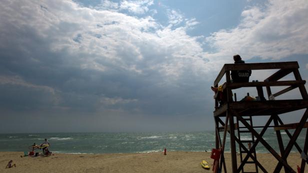 Ein Rettungsschwimmer sitzt auf einem Turm an einem bewölkten Strand.