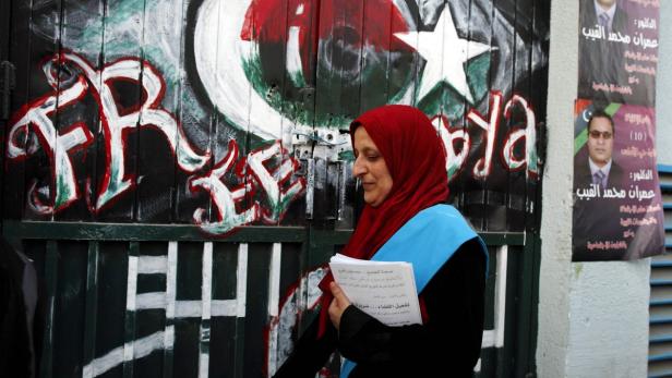 Eine Frau mit Kopftuch geht an einer Wand mit Graffiti und Wahlplakaten vorbei.