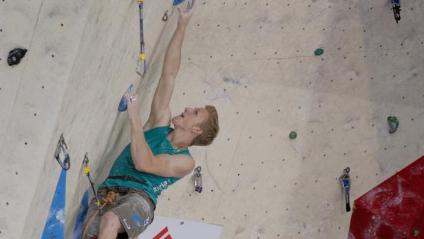 Ein Mann klettert an einer Kletterwand mit verschiedenen Griffen und Sicherungsausrüstung.