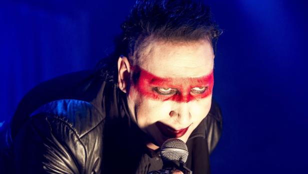 Marilyn Manson mit roter Farbe im Gesicht singt in ein Mikrofon.
