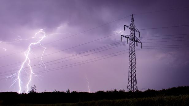 Blitze zucken neben einem Strommast am dunklen Himmel.