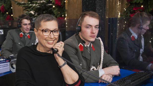 Eine Frau telefoniert, während junge Männer in Uniformen im Hintergrund sitzen.