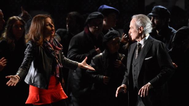 Eine Frau gestikuliert auf der Bühne, während ein älterer Mann im Anzug daneben steht.