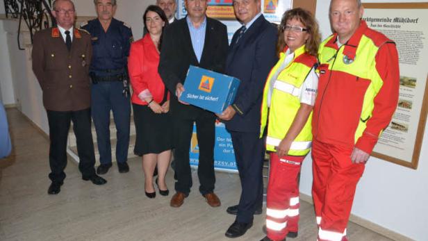 Eine Gruppe von Personen verschiedener Organisationen posiert mit einer blauen Kiste, auf der „Sicher ist sicher!“ steht.