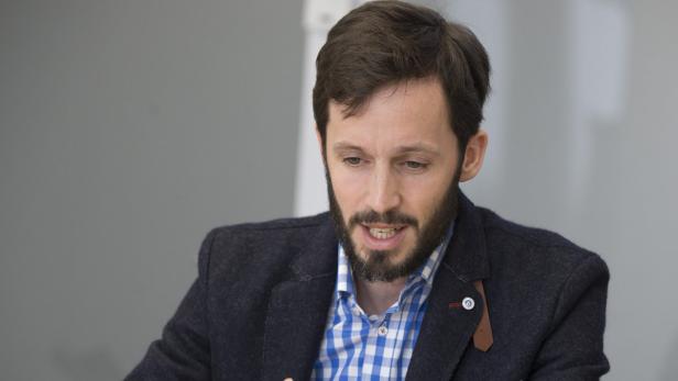 Ein Mann mit Bart und blauem Hemd spricht.