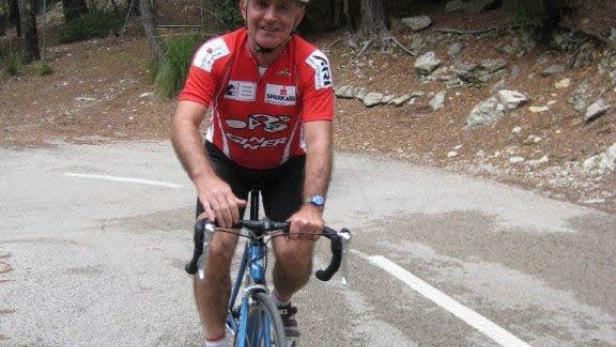 Ein Mann mit Helm fährt mit einem Rennrad auf einer asphaltierten Straße.