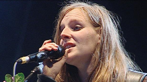 Eine Frau mit blonden Haaren singt in ein Mikrofon.