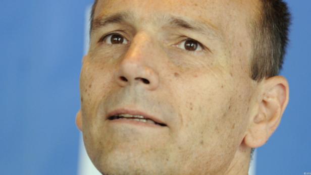 Nahaufnahme eines Mannes mit braunen Augen vor blauem Hintergrund.