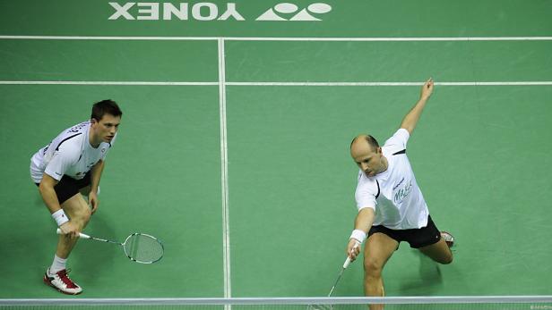 Zwei Badmintonspieler während eines Spiels auf einem grünen Platz.