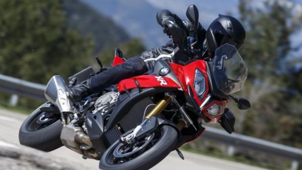Ein Motorradfahrer fährt mit einer roten BMW S 1000 XR auf einer kurvigen Straße.