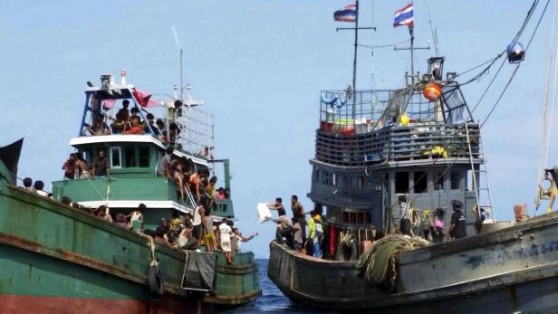 Zwei überfüllte Boote auf dem Wasser, eines davon mit thailändischer Flagge.