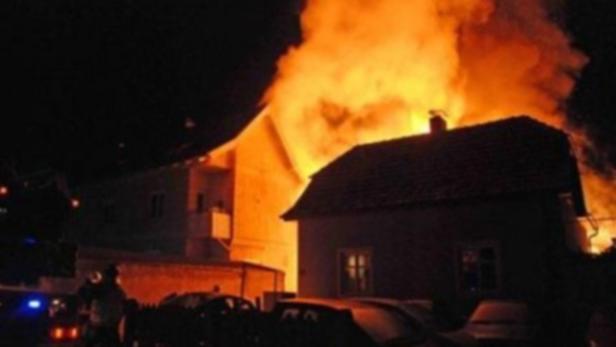 Ein Haus steht in Flammen, während im Vordergrund Autos geparkt sind.