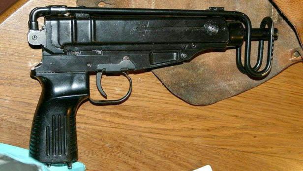 Eine schwarze Maschinenpistole vom Typ Škorpion vz. 61 liegt auf einem Holztisch.